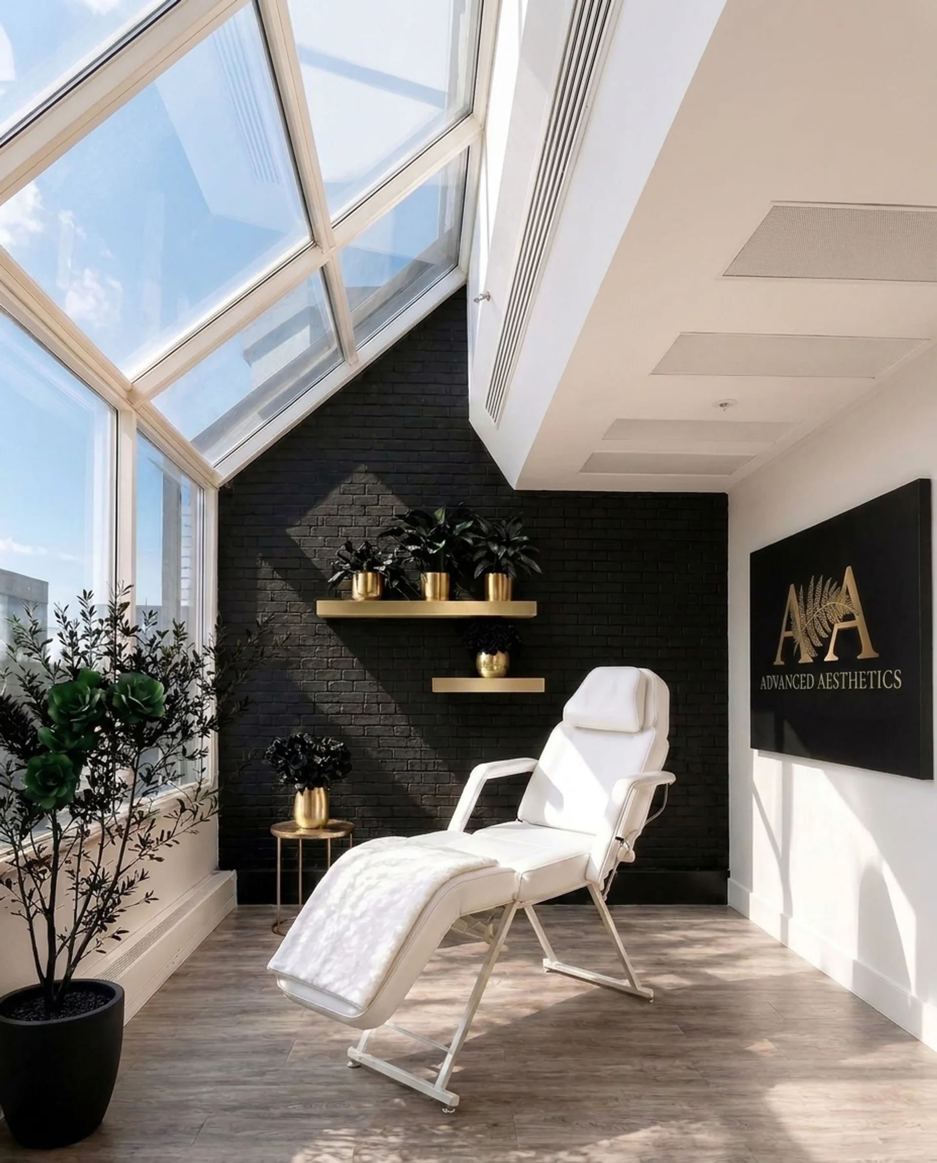 The Advanced Aesthetics treatment room, black brick, gold shelves, black roses and the fern logo